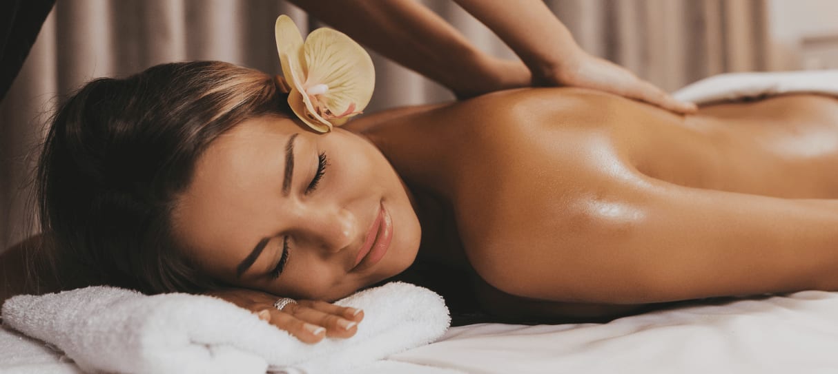 Gästin erhält eine entspannende Rückenmassage, eine Orchideenblüte im Haar