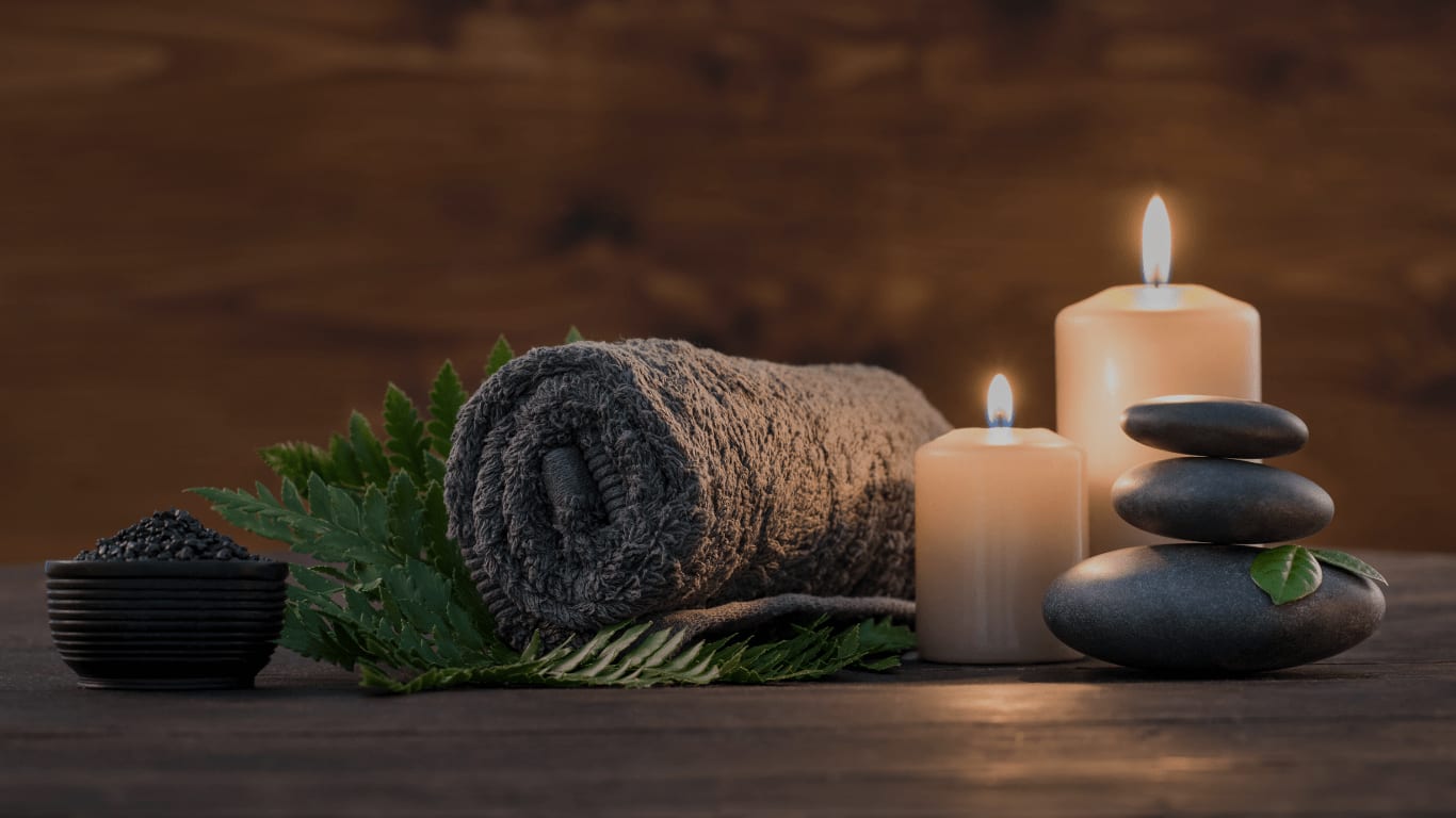Zusammengerolltes Spa-Handtuch mit brennenden Kerzen und heißen Steinen auf Holzuntergrund